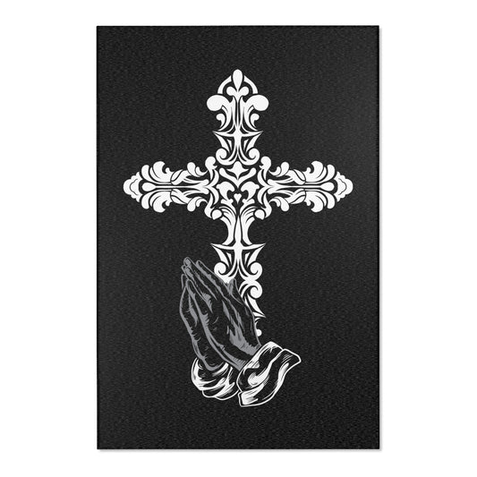 A rectangular area rug with a floral cross design above a praying hands motif on a dark background.