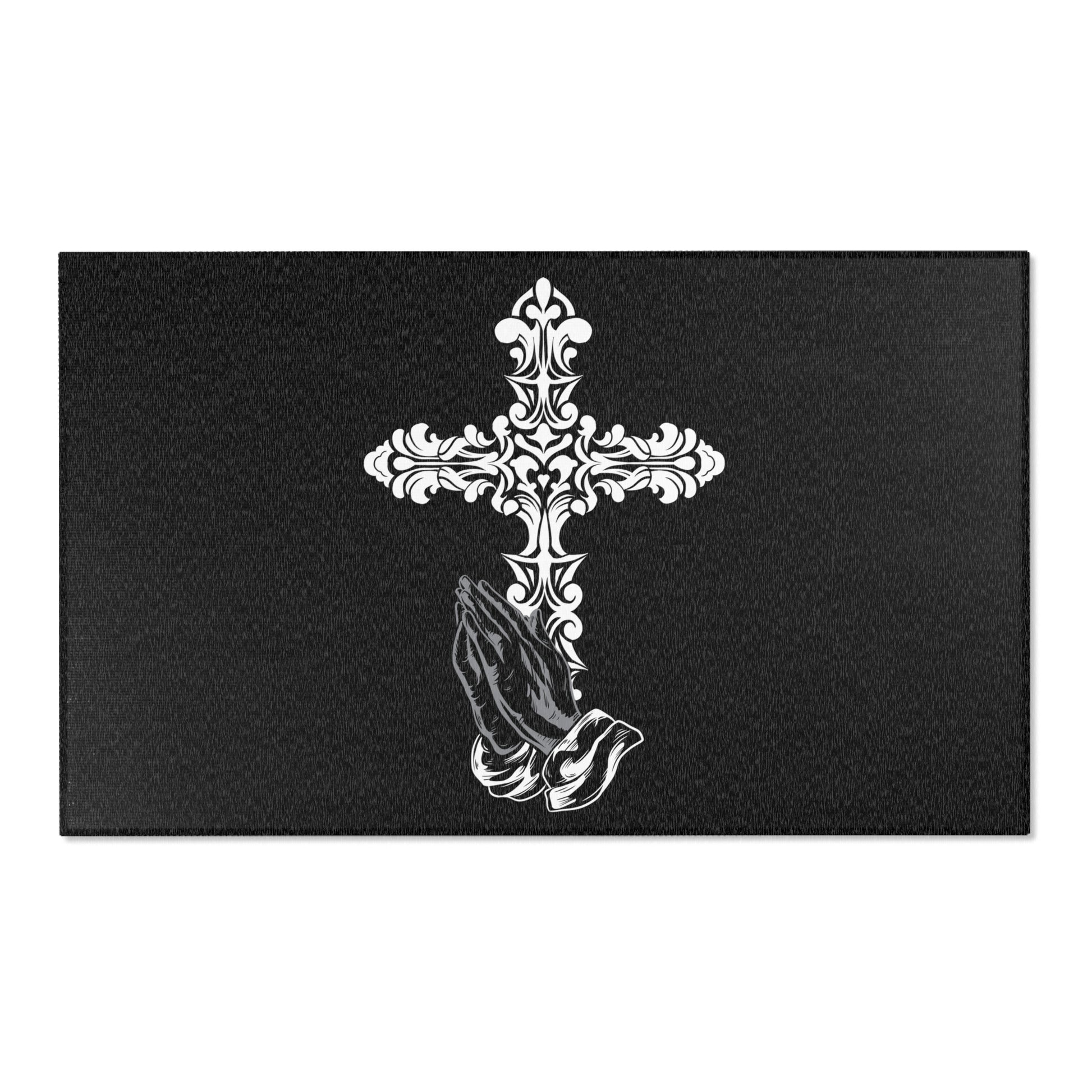A rectangular area rug with a floral cross design above a praying hands motif on a dark background.